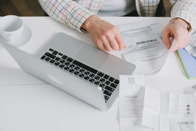 Person reviewing printed bills beside a laptop