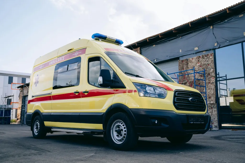 Yellow ambulance with a red stripe parked beside a building