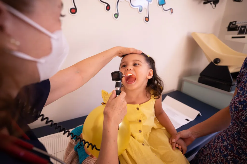 Physician shining a light into a young girl's open mouth during an exam