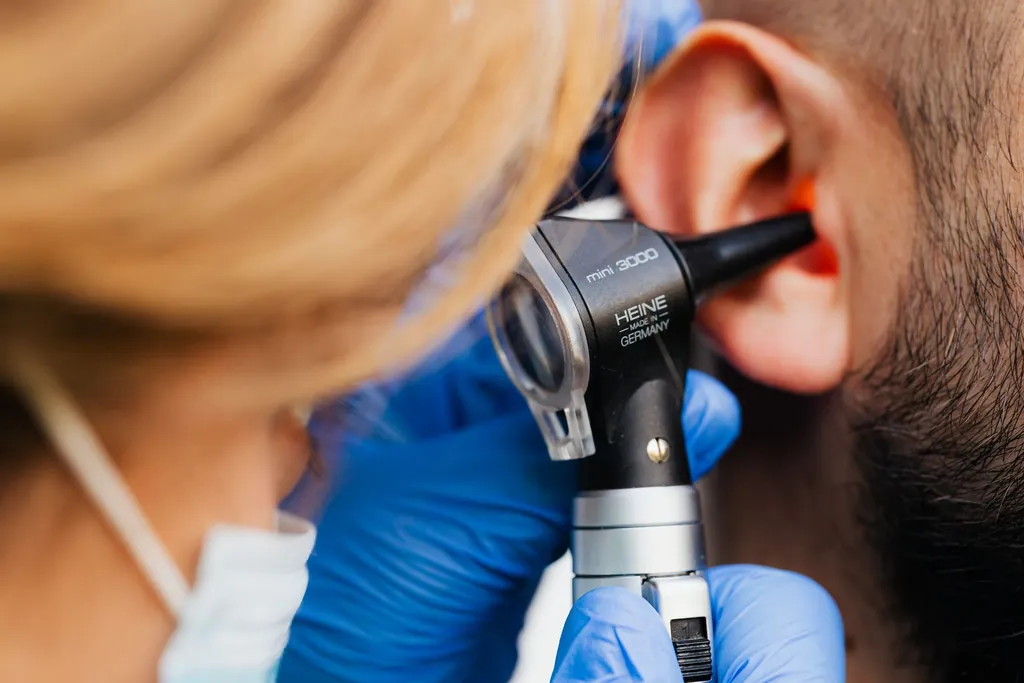 Clinician in blue gloves examining a patient's ear with an otoscope