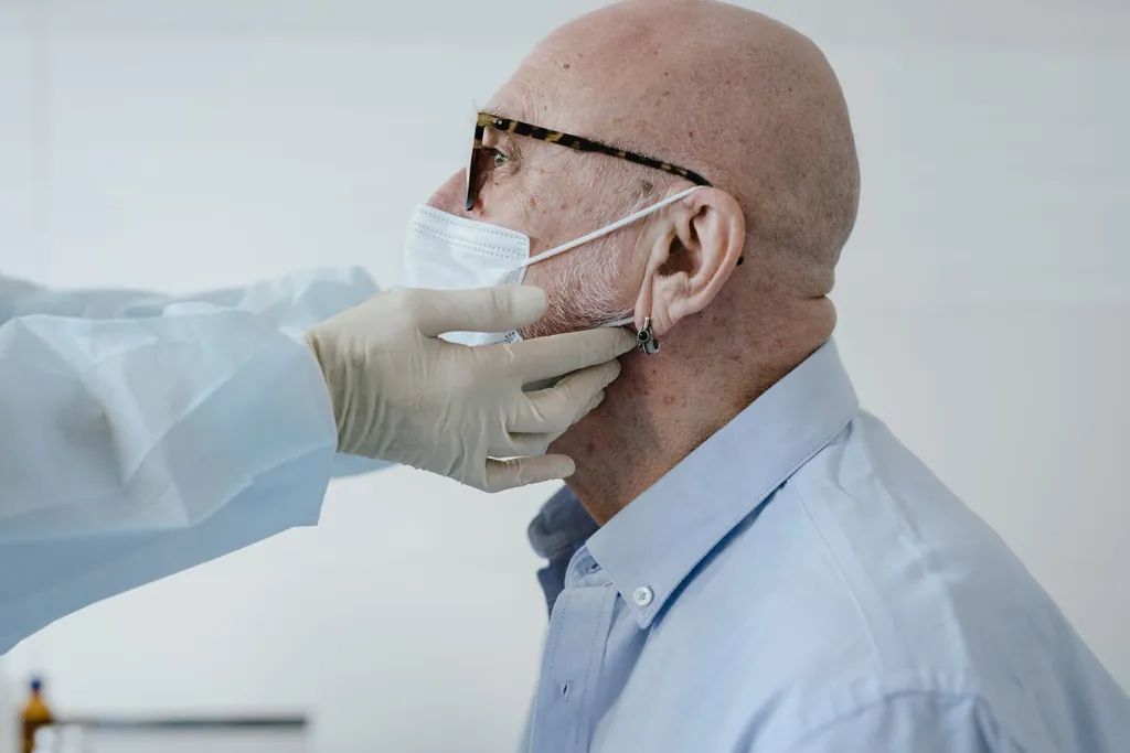 Gloved clinician examining an older man's neck during a check-up