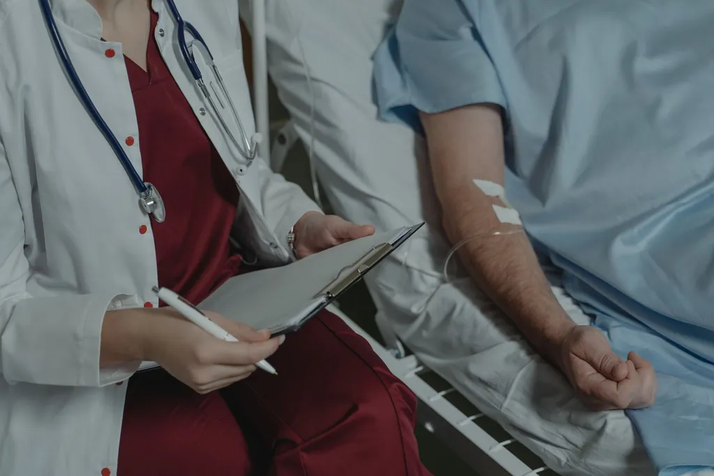 Clinician with a clipboard beside a patient receiving an IV infusion