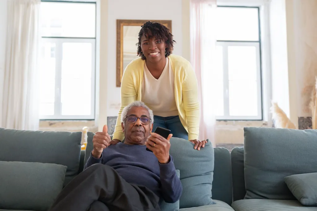 Caregiver smiling with an older man on a sofa at home