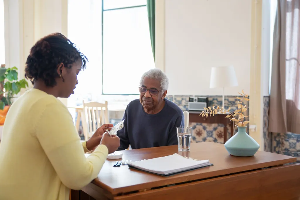 Caregiver preparing medicine for an older man at a table