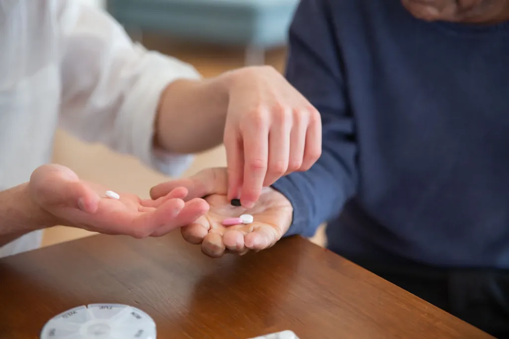 Caregiver handing an older person their tablets at the table