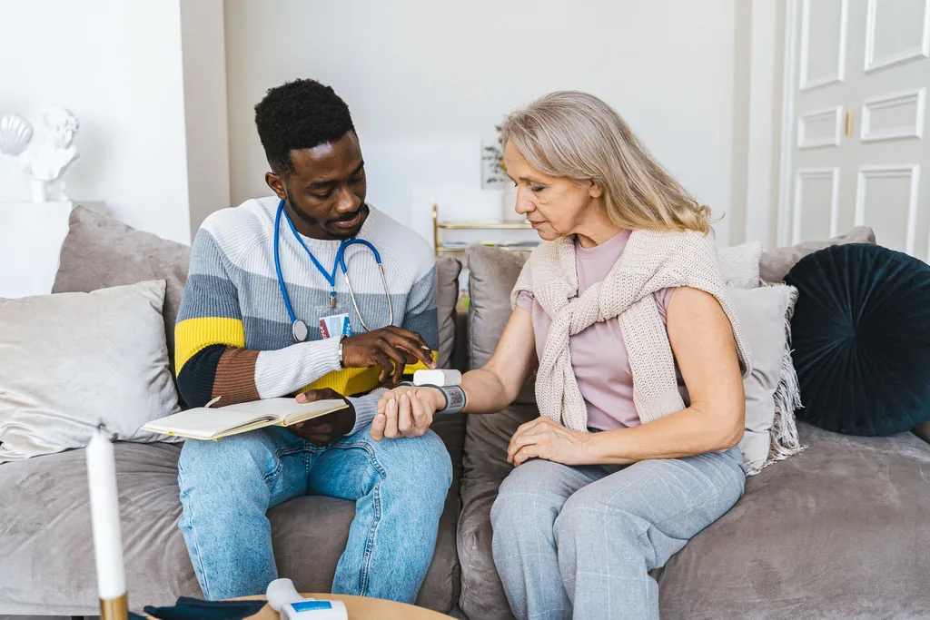 Home health clinician taking notes with a woman on her sofa