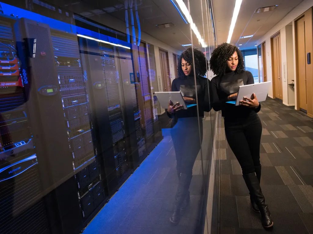 Woman with a laptop walking along a row of servers