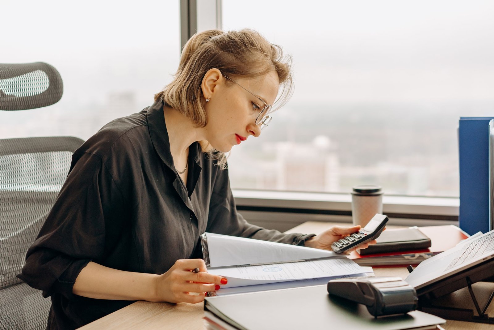 Billing specialist working through paperwork with a calculator at an office desk