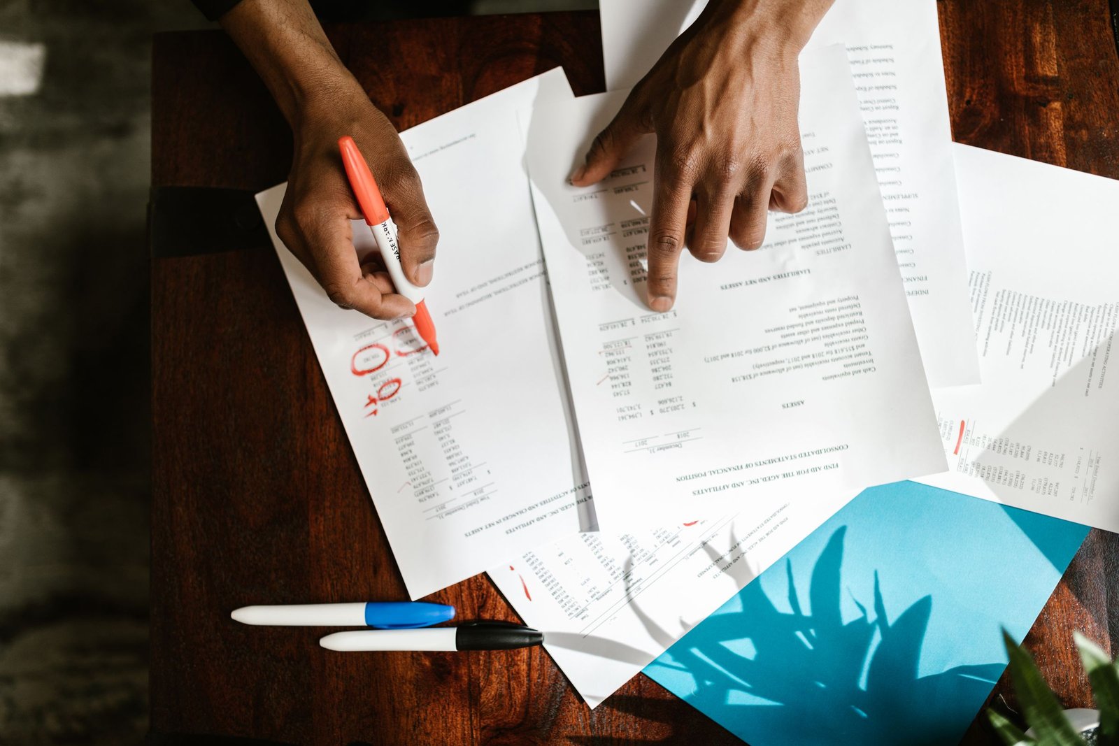 Hands marking up printed claim documents with a red marker on a desk