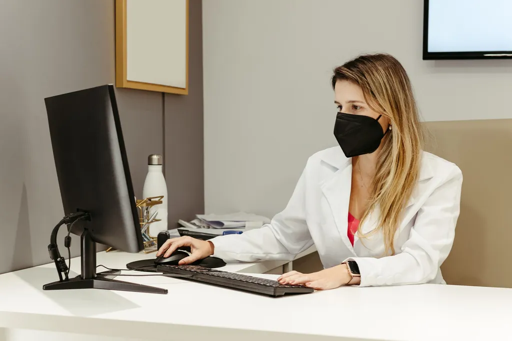 Practice staff member in a white coat working at a computer in a clinic office