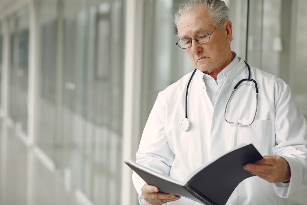 Older doctor in a white coat reading clinical records in a hallway