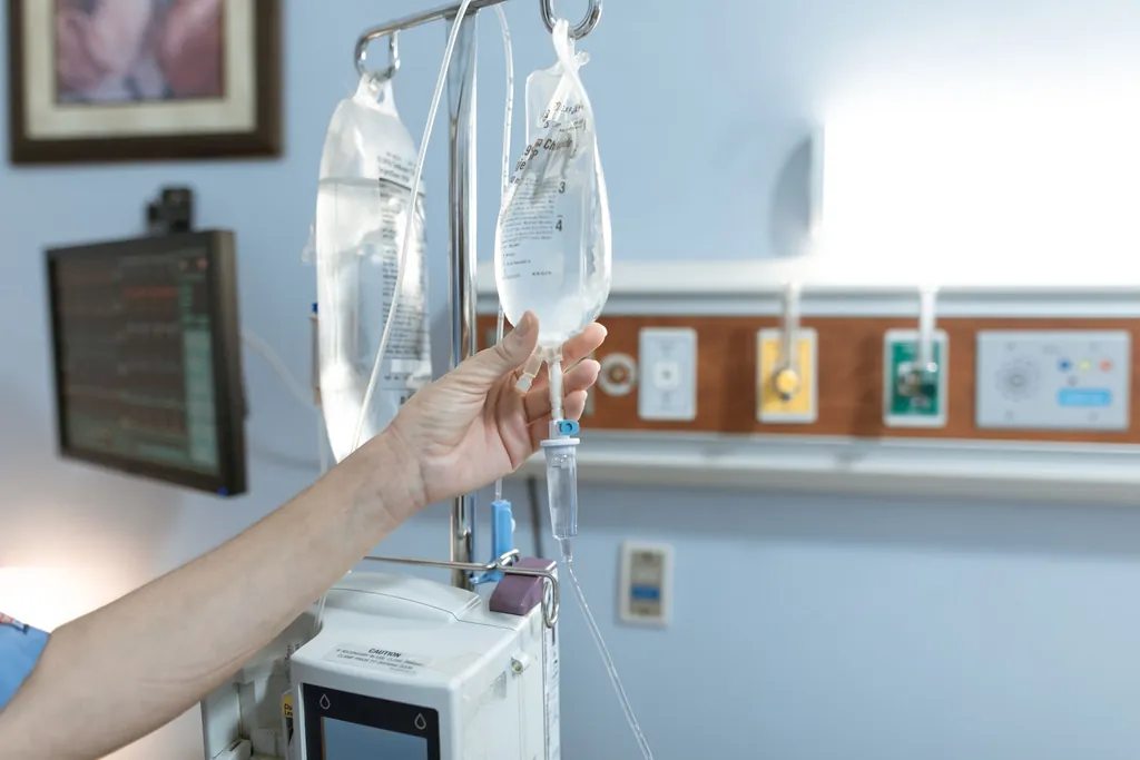 Clinician checking an IV infusion bag beside a hospital bed
