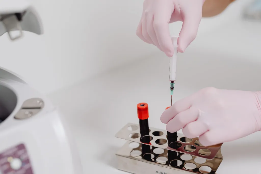 Gloved hands with a pipette above blood sample tubes in a rack