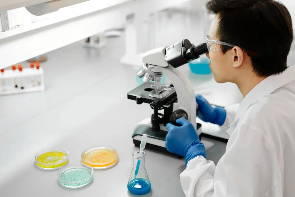 Scientist in a lab coat using a microscope beside petri dishes