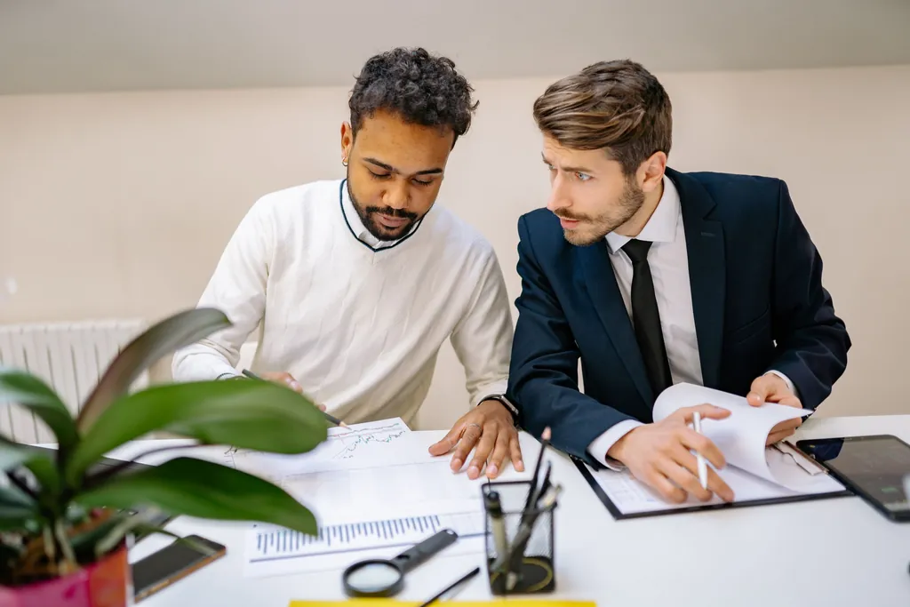 Two colleagues reviewing printed reports and charts at an office desk