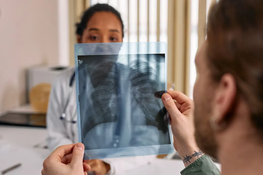 Masked clinician holding up a chest X-ray while talking with a patient
