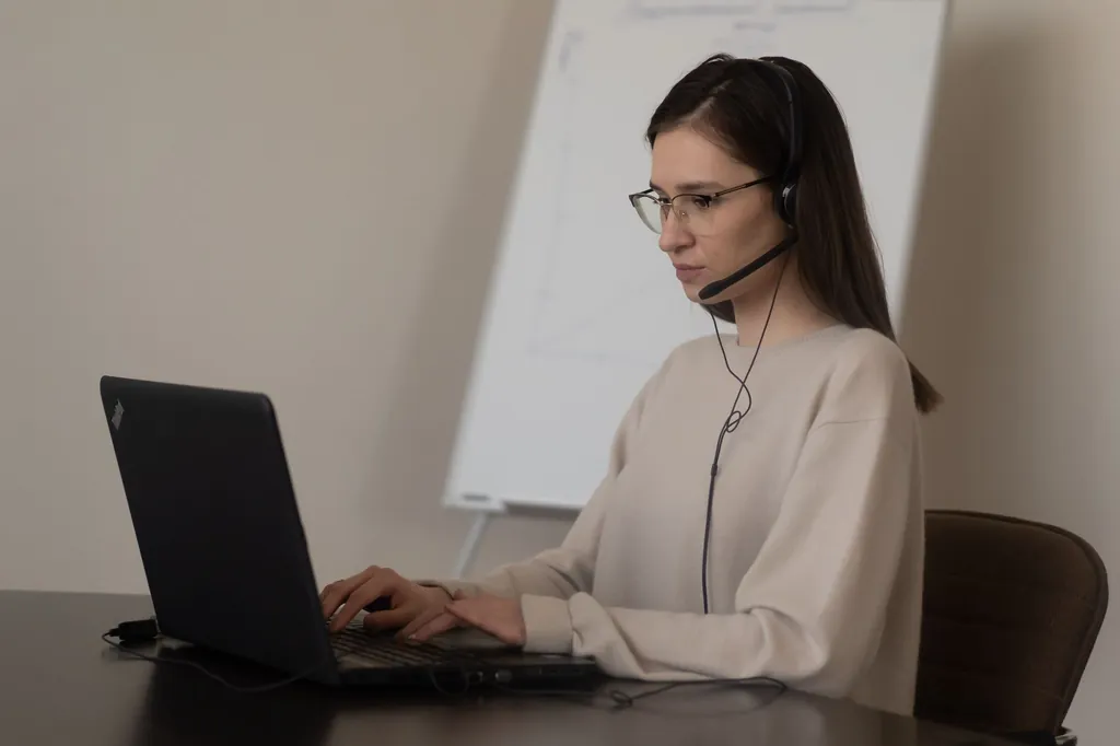 Woman wearing a headset typing on a laptop at her desk