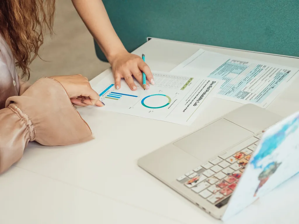 Two people pointing at printed charts on a desk next to a laptop