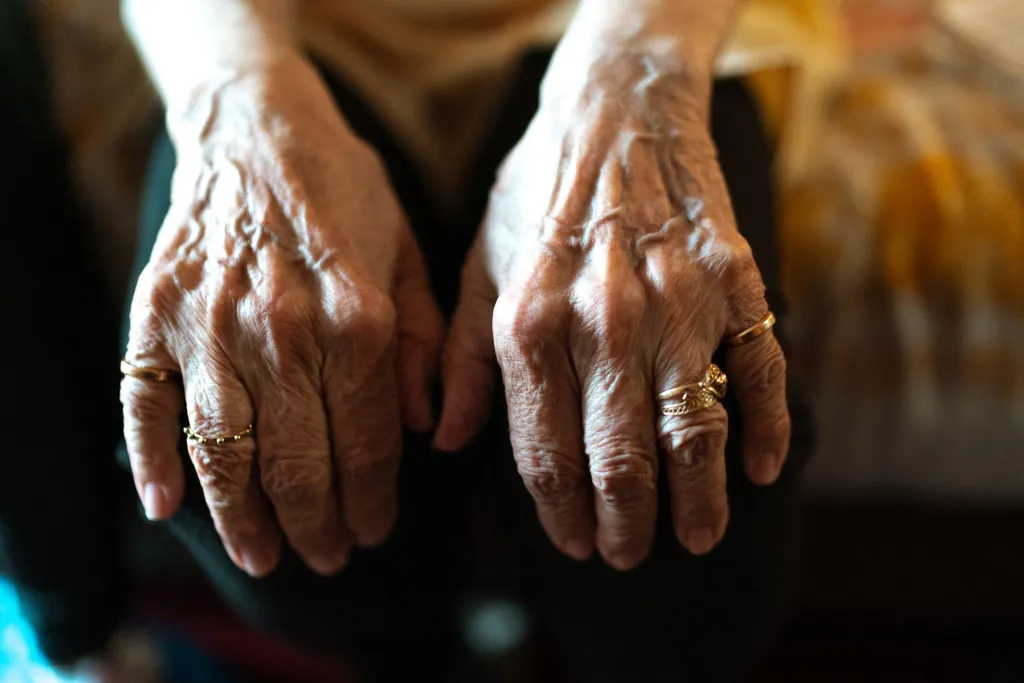 Close-up of an older person's hands with rings resting in their lap
