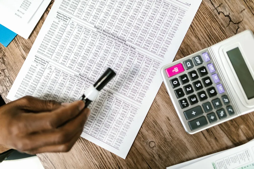 Hand holding a marker over a printed spreadsheet beside a calculator
