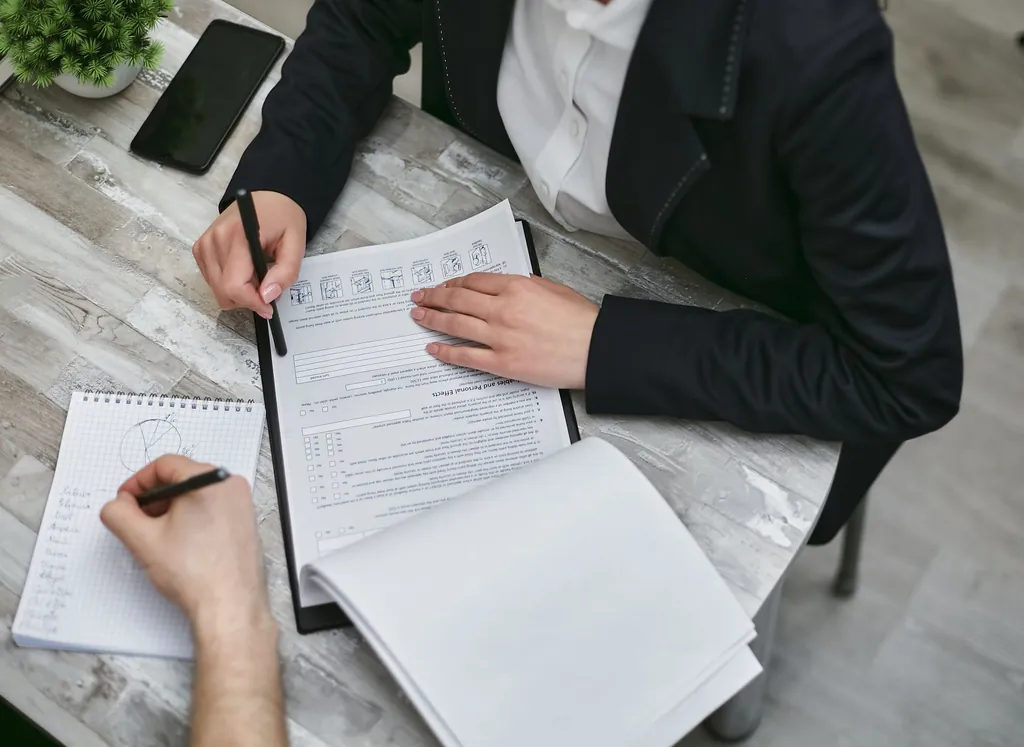 Two people at a desk filling in and checking paper forms