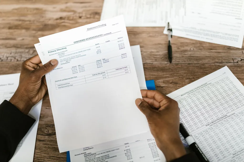 Hands holding printed forms over a desk covered in paperwork