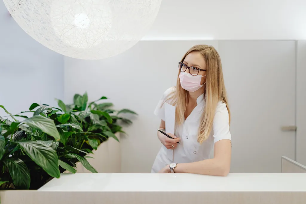 Receptionist in a face mask standing at a clinic front counter