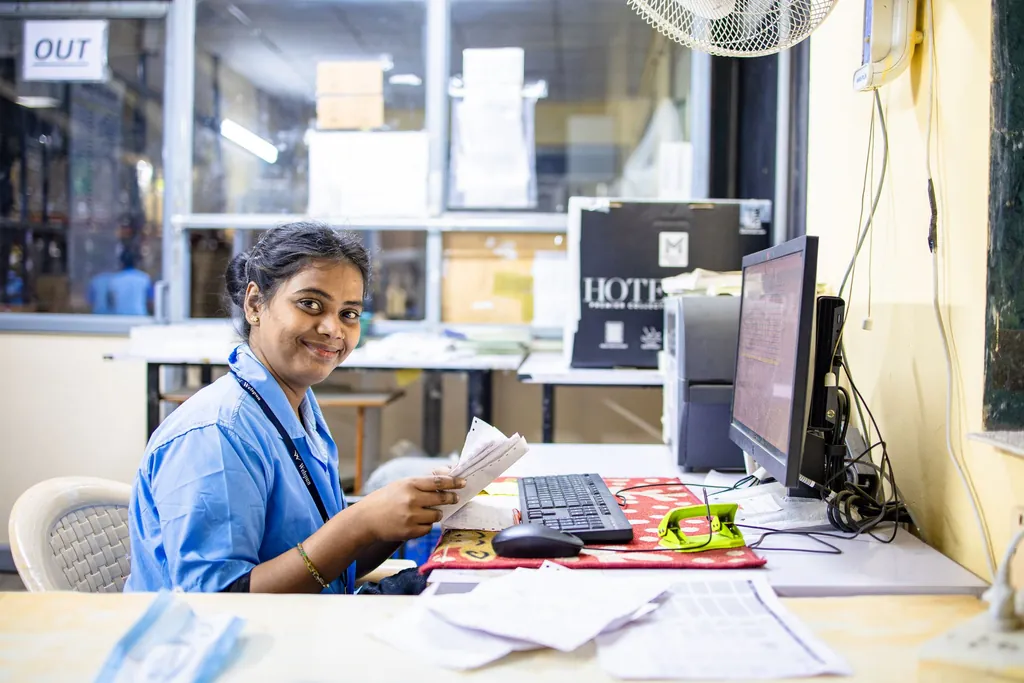 Smiling staff member in scrubs working at a desk with papers and a computer