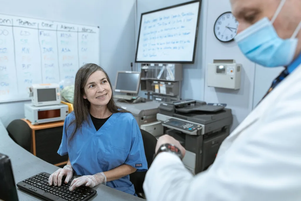 Nurse in scrubs at a hospital workstation smiling at a doctor beside her