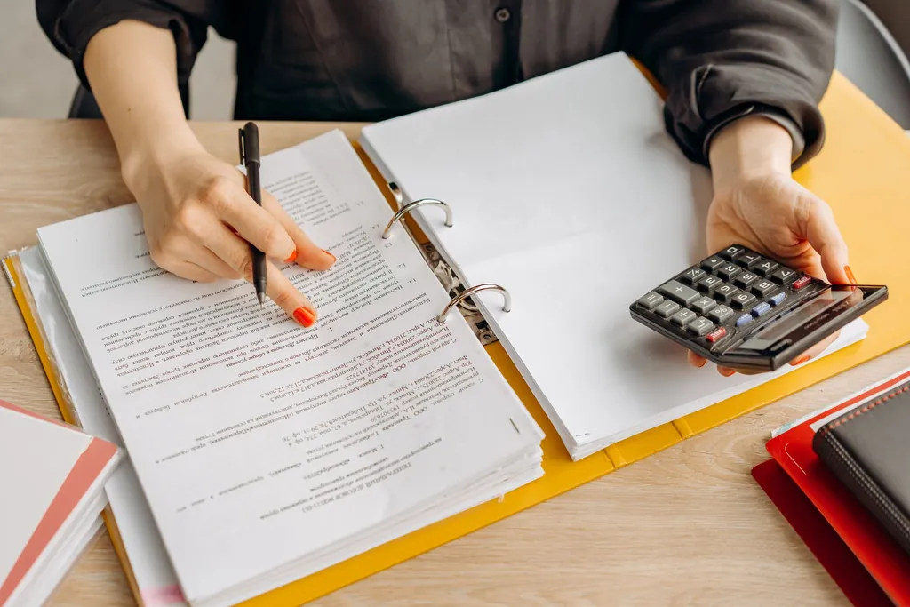 Person checking a statement in a binder with a calculator and pen