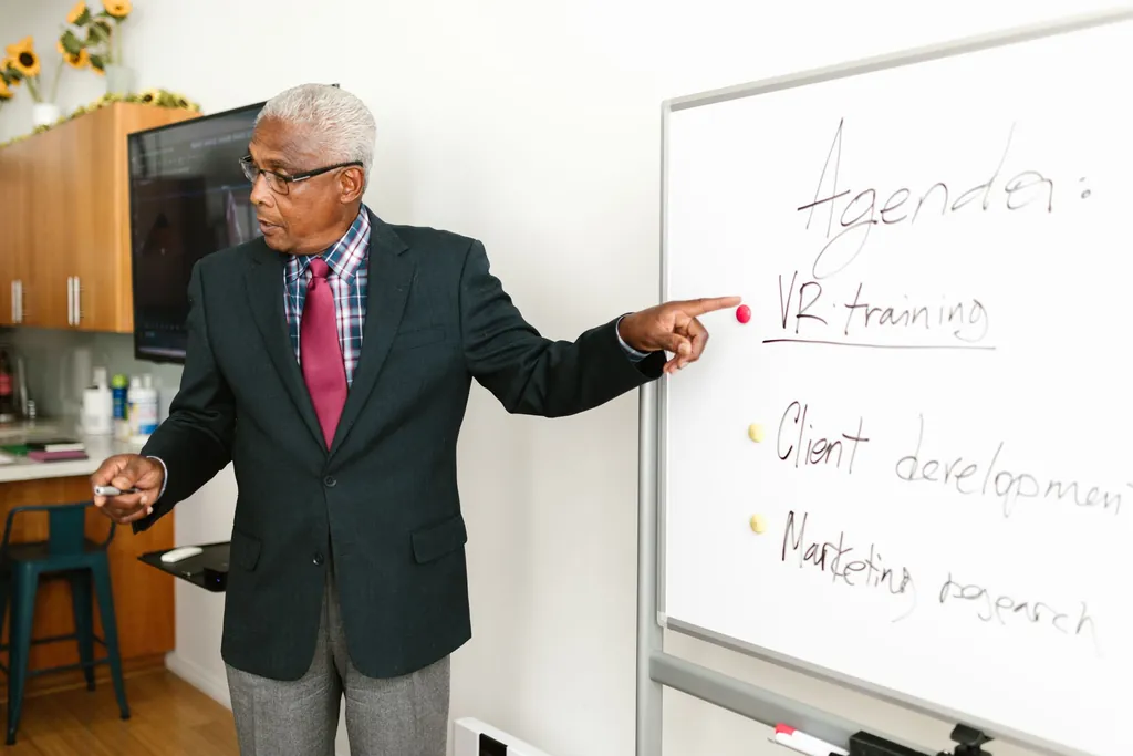 Older man in a suit pointing to notes on a whiteboard