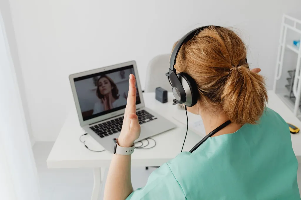 Clinician wearing a headset on a video call with a patient on her laptop