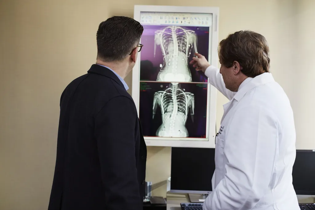 Physician pointing to an X-ray on a light box while talking with a man in a suit